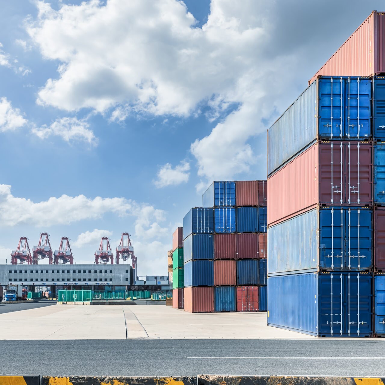 Stacked containers and pavement and buildings at port. Commercial pier landscape on a sunny summer day